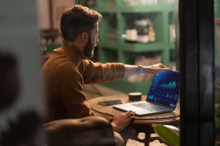 Modern businessman reviewing analytics dashboard and performance metrics on laptop. Professional analyzing digital data visualization in cozy cafe environment.